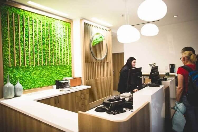 A hotel reception desk with a moss wall and guests speaking to an employee