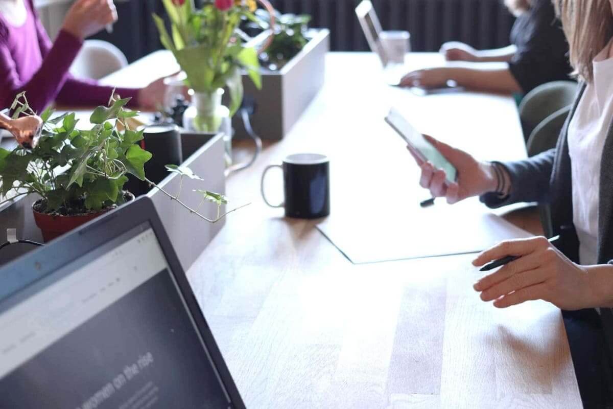 Plants on a boardroom table where people are on their phones and laptops 