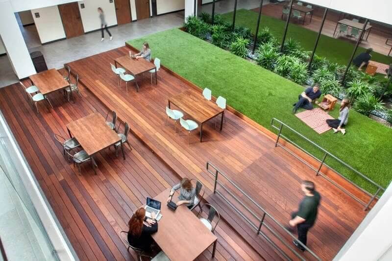 An open space with people sitting at tables, surrounded by plants